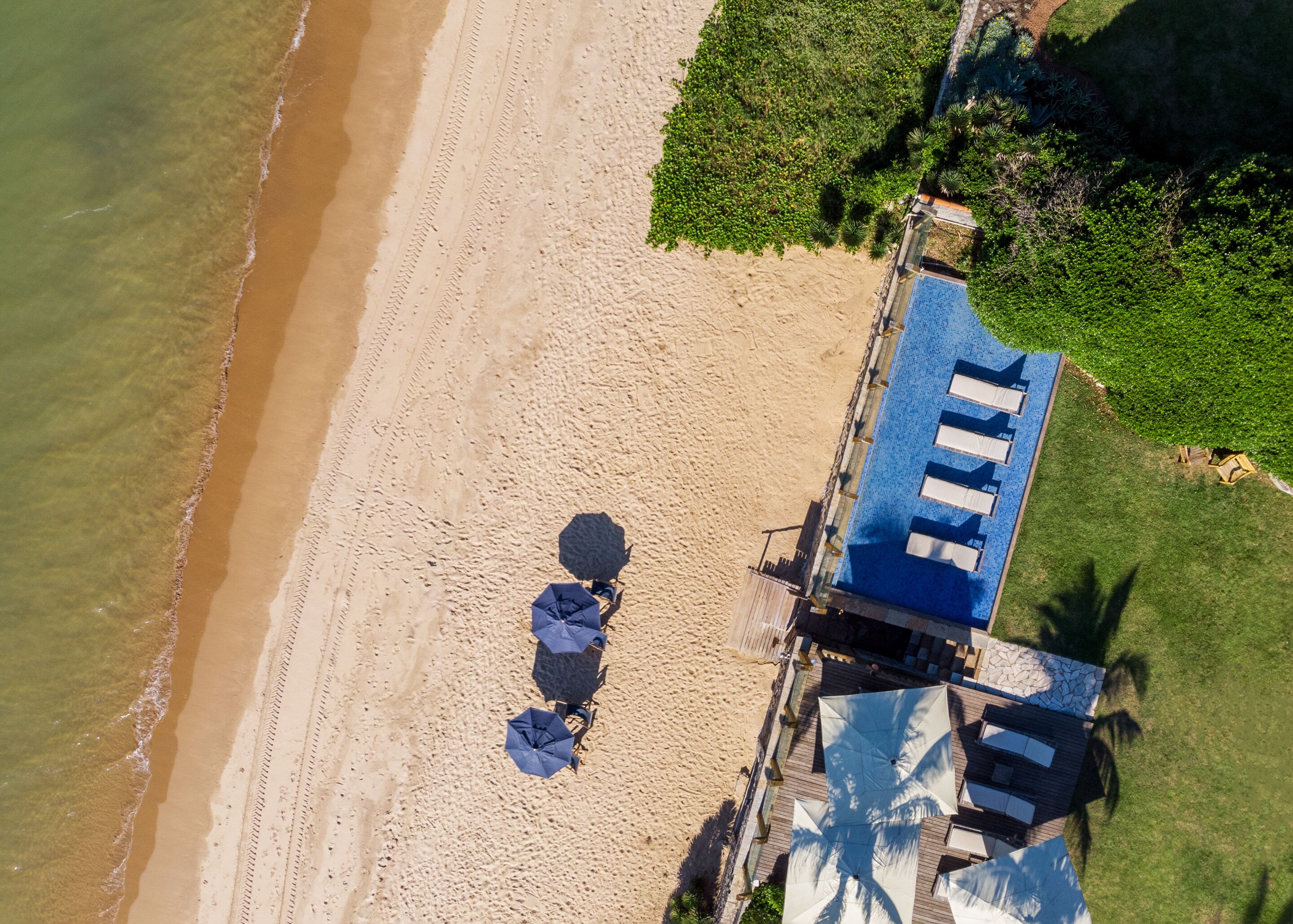 An aerial view of a beachside property with a pool area, a beach, and a garden.