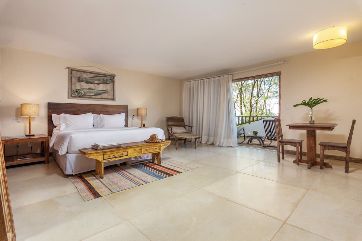 A bedroom with a bed, bedside tables, a chair, a small table, and a window with curtains.