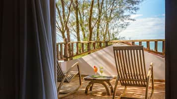 A balcony with wooden chairs and a table, overlooking a body of water and trees.