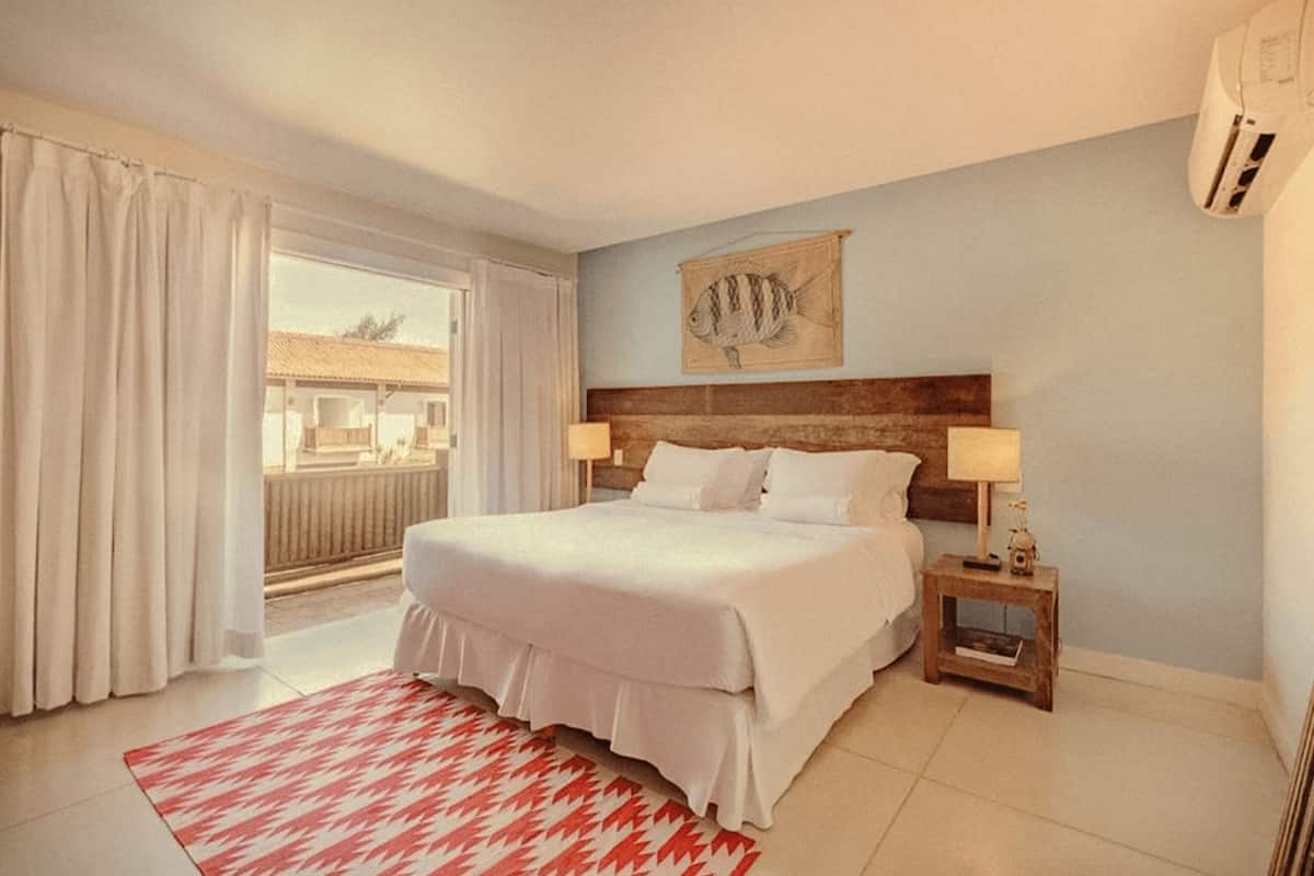 A hotel room with a bed, a nightstand with a lamp, a wall-mounted fish artwork, and a view through a window.