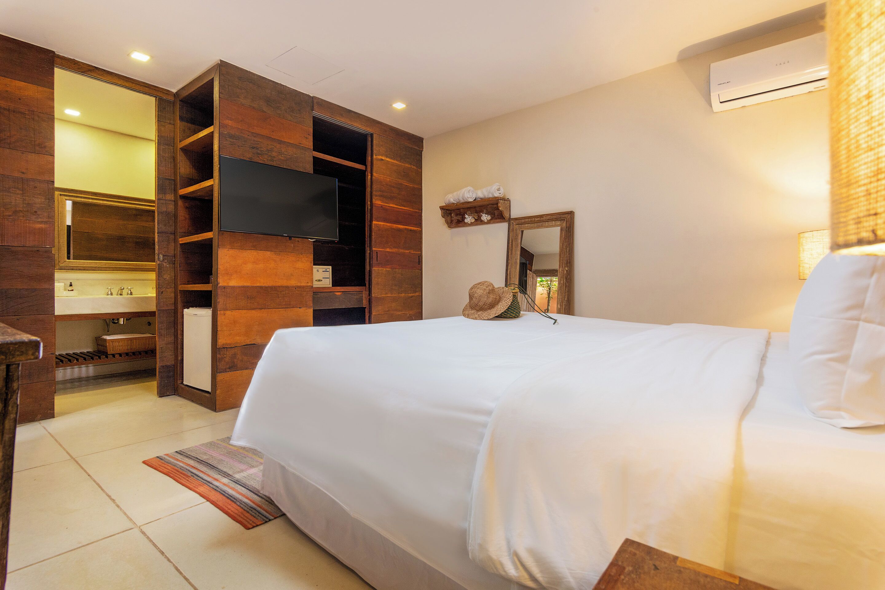 A hotel room with a large bed, a wooden wardrobe, a television, a mirror, and an air conditioning unit.