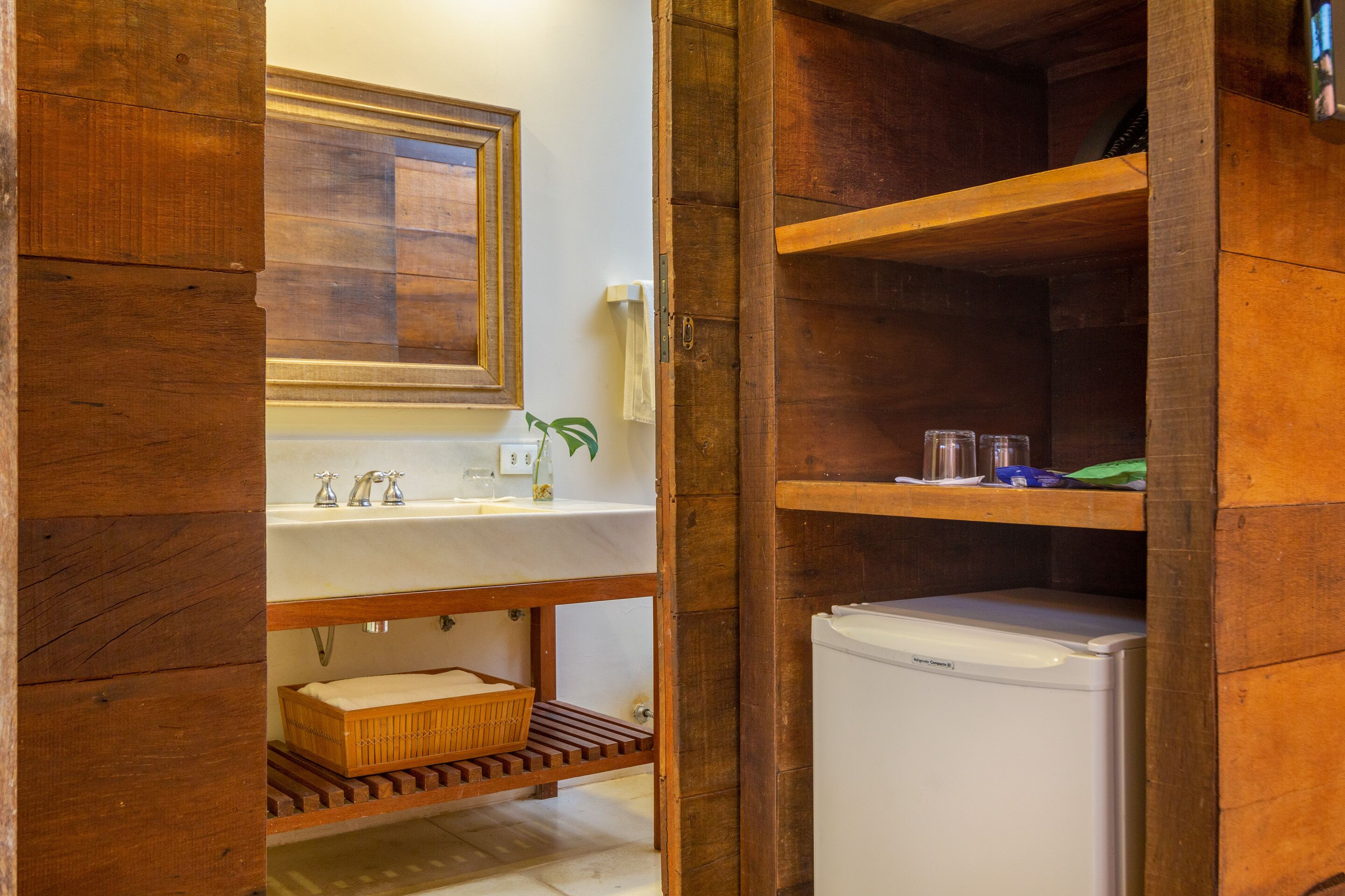 Bagno con struttura in legno, dotato di lavandino, specchio e un piccolo frigorifero.