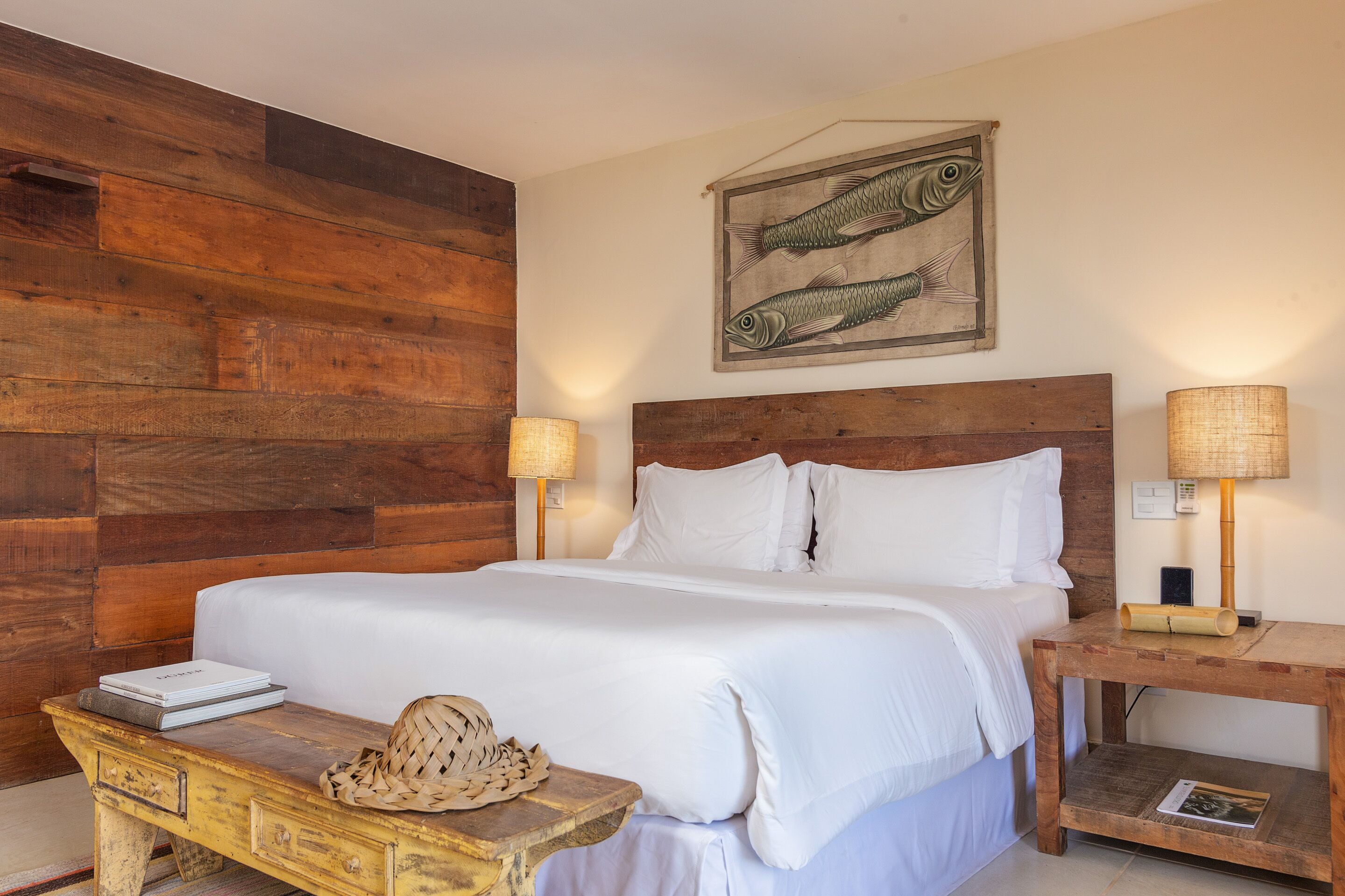 A neatly made bed with white linens, a wooden headboard, and a wall-mounted fish painting.