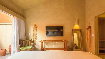 Un dormitorio con una cama, una mesita de noche de madera, un espejo, un televisor montado en la pared y una ventana con cortinas.