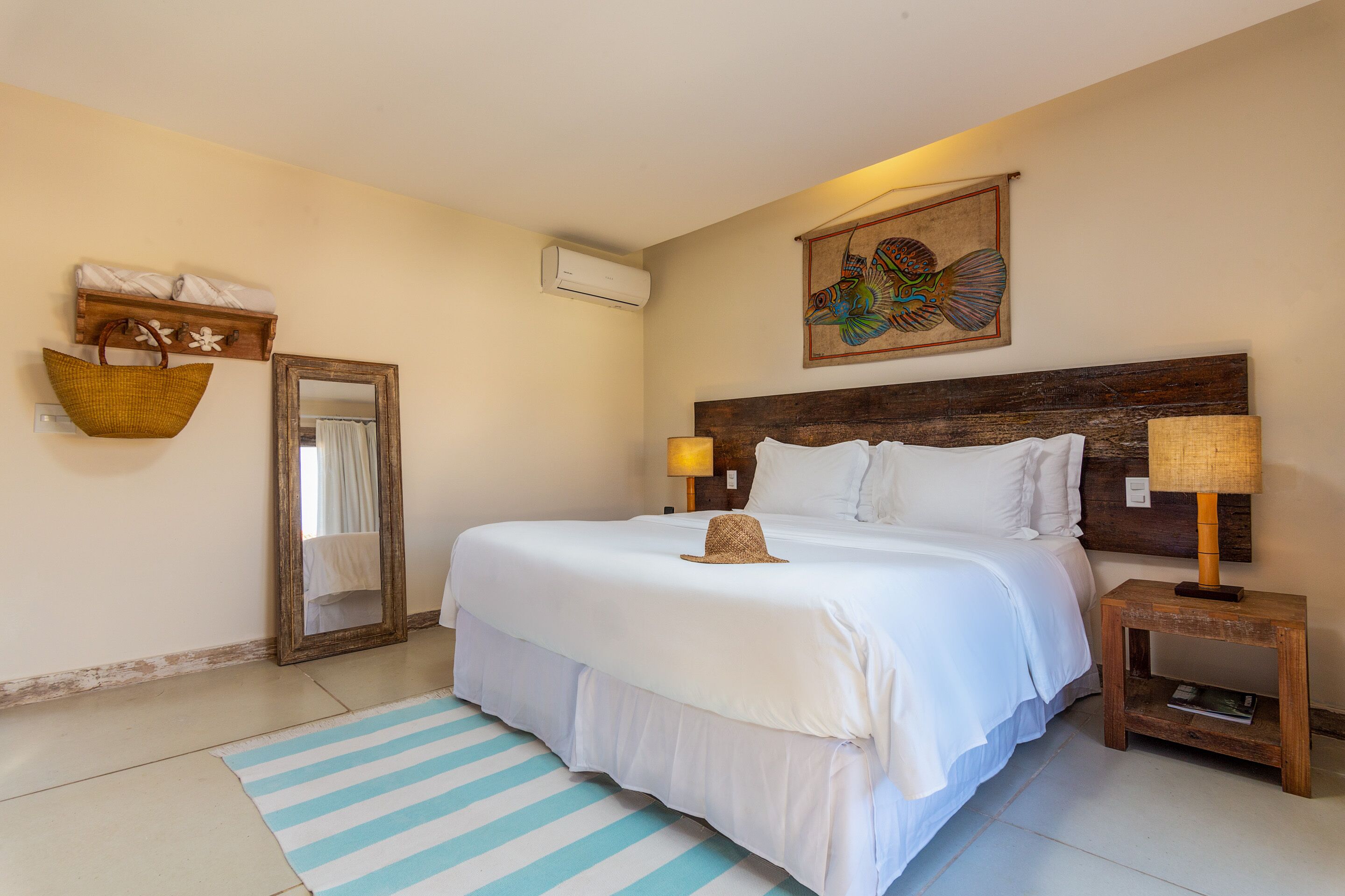 Een slaapkamer met een groot bed, een houten hoofdbord, een nachtkastje met een lamp, een wandairconditioner, een spiegel en een decoratieve wandversiering.