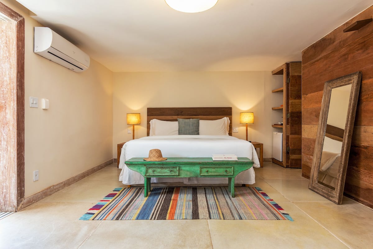 A bedroom with a bed, bedside lamps, a green bench, a striped rug, and a wooden wardrobe.