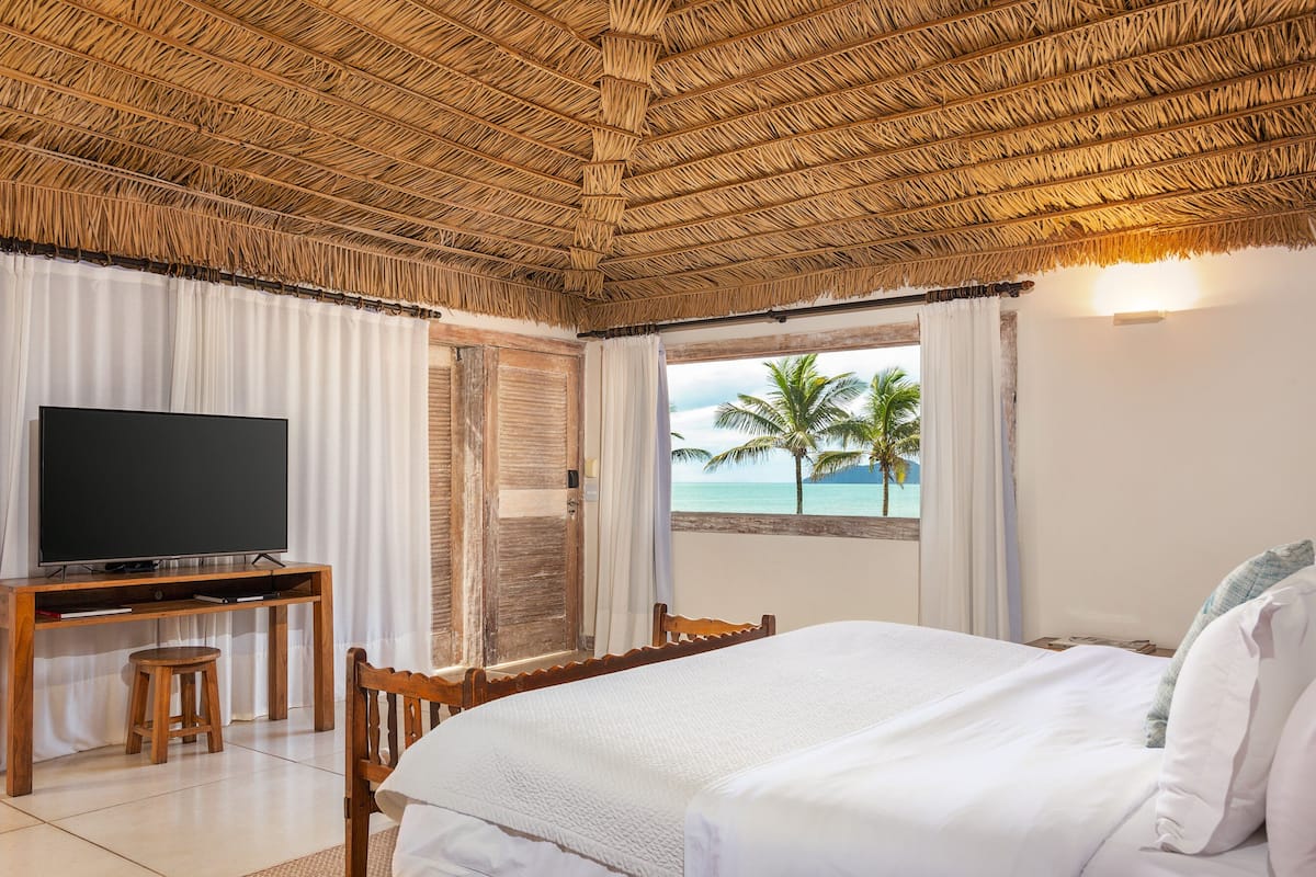 A room with a bed, a TV, a desk, and a view of the ocean.