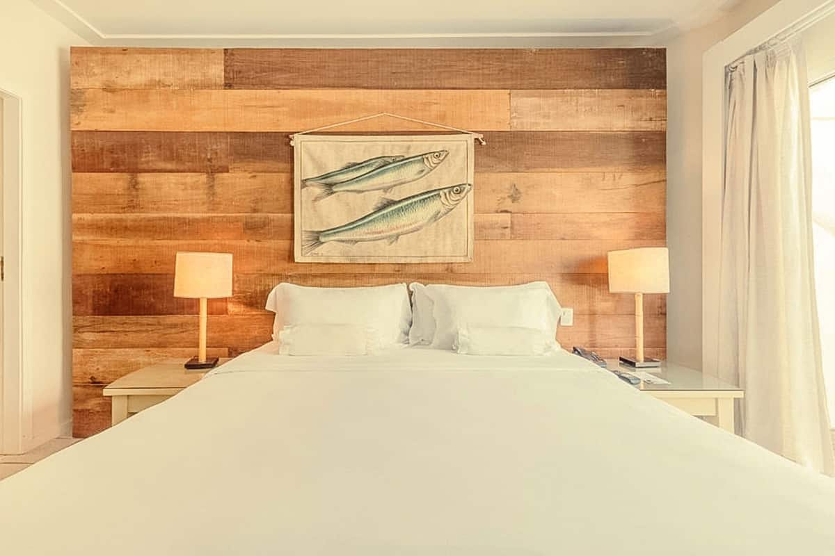 A hotel room with a wooden wall, a bed with white linens, two bedside tables with lamps, and a fish painting above the bed.