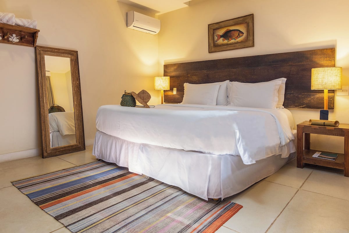 A hotel room with a large bed, a wooden headboard, a mirror, a lamp, and a framed picture on the wall.