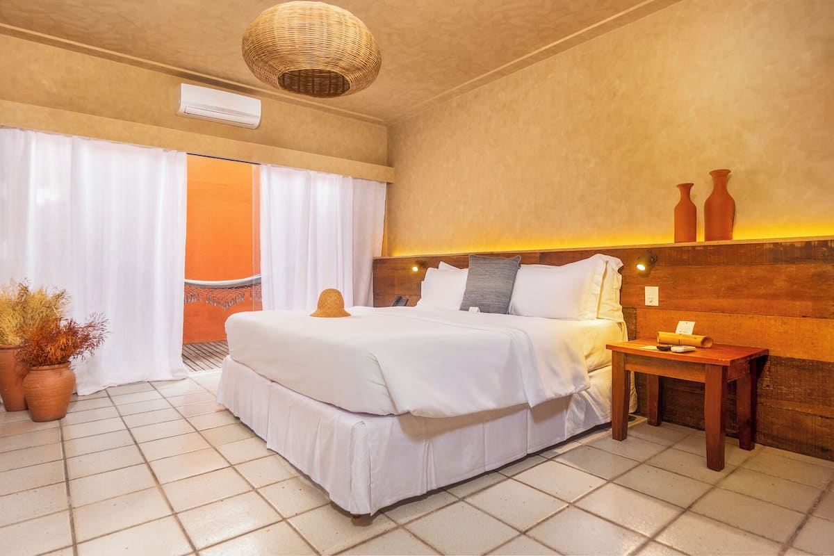 A hotel room with a bed, a nightstand, a wicker ceiling light, and a view of the outside.