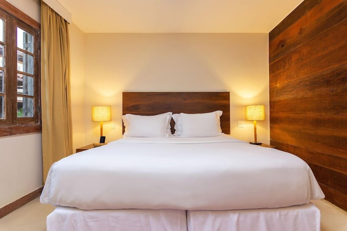 A large bed with white linens, two bedside lamps, and a wooden headboard.
