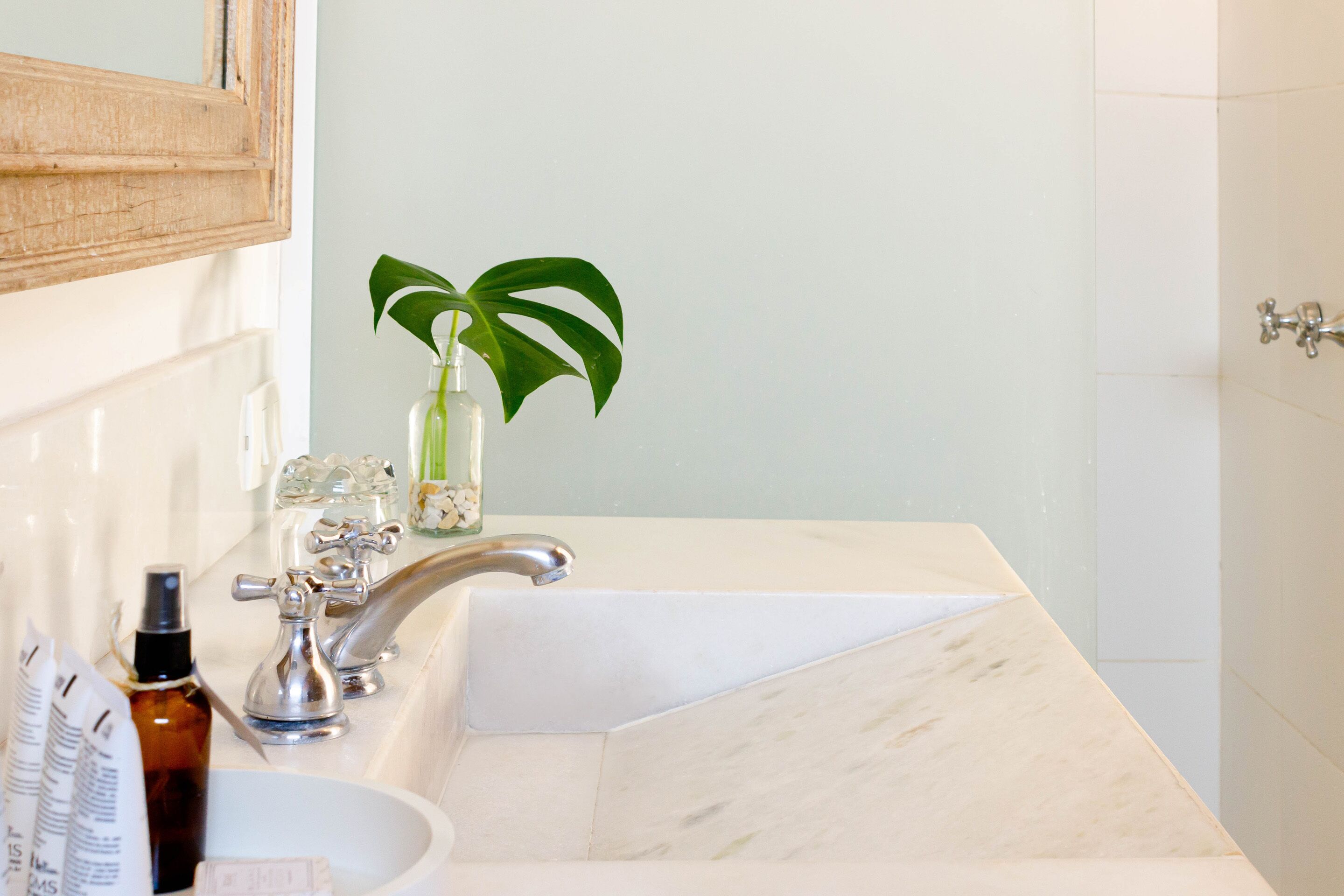 A bathroom with a marble sink, a mirror, and a plant.