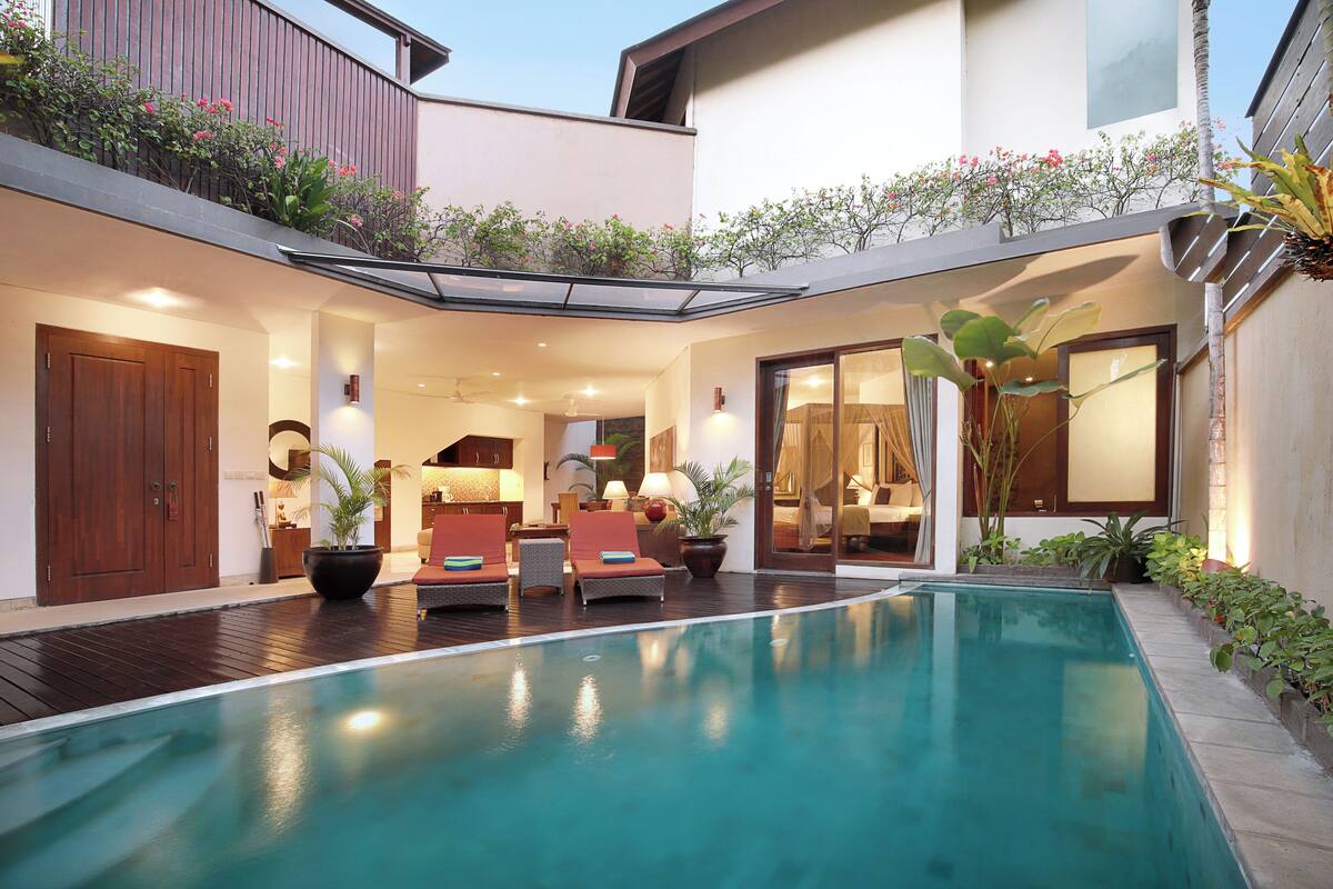 A modern outdoor pool area with a wooden deck, lounge chairs, and potted plants.
