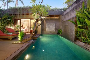 A swimming pool with a wooden deck, lounge chairs, and tropical plants.