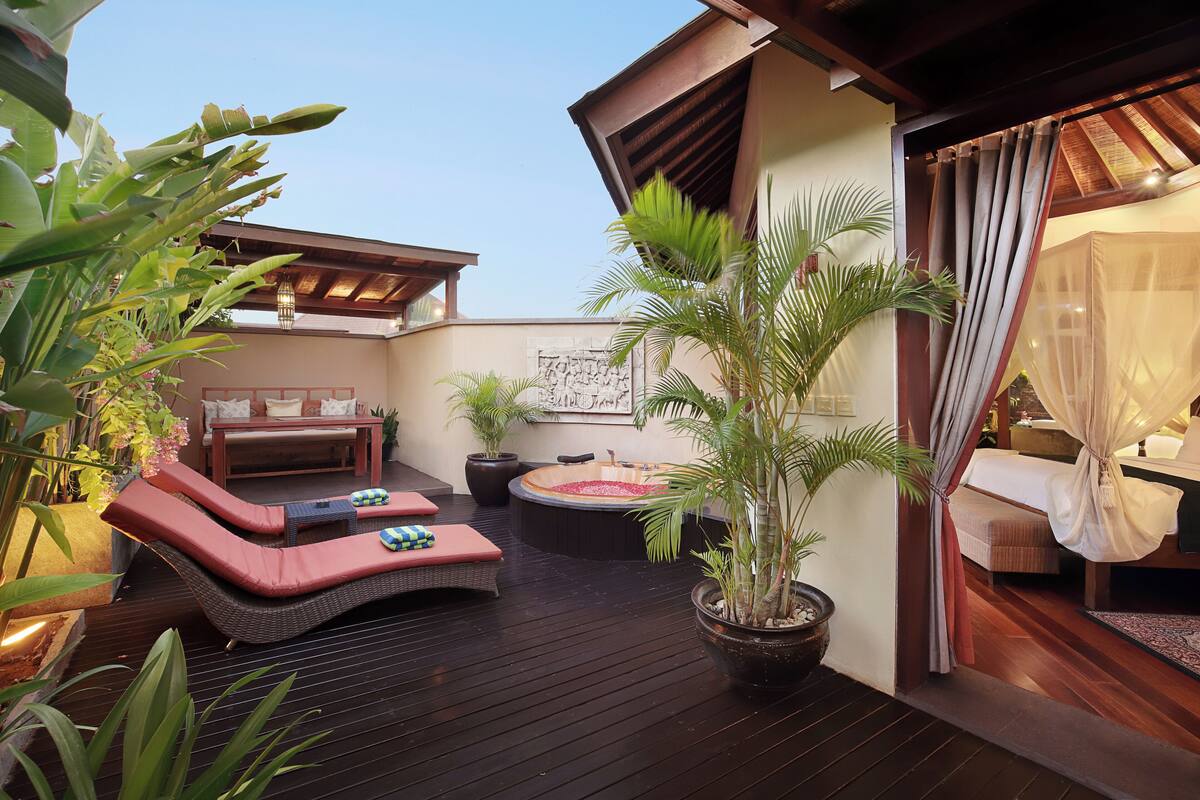 A wooden deck with a hot tub, lounge chairs, and potted plants.