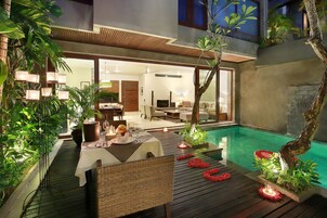 Uma área de refeições moderna ao ar livre, com piscina, deck de madeira e vegetação exuberante.