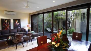 A spacious living room with a large dining table, comfortable seating, and a view of a swimming pool.