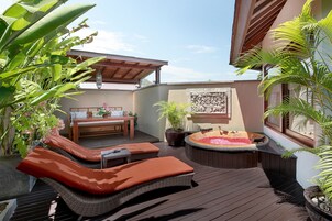 Um deck com uma banheira de hidromassagem, espreguiçadeiras e uma mesa com um vaso de planta.