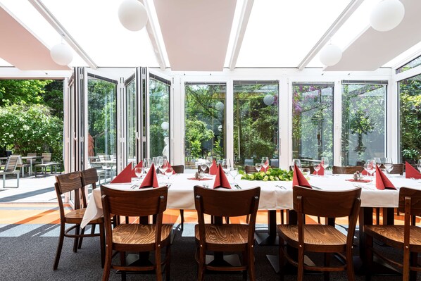 A restaurant with large glass windows, wooden chairs, and white tablecloths. - Hotel Grenzfall Berlin (Berlin)