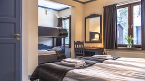 Quarto de hotel com beliche, escrivaninha, cadeira, espelho e janela com cortinas.