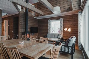 A wooden interior with a dining table, chairs, a sofa, and a fireplace. - Trillevallen Högfjällshotell (Undersaker)