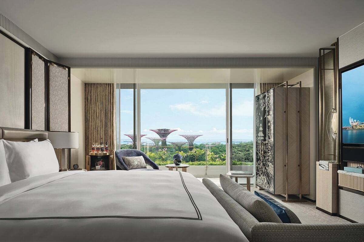 A hotel room with a large bed, a seating area with a view of greenery and a distinctive building, and a television.