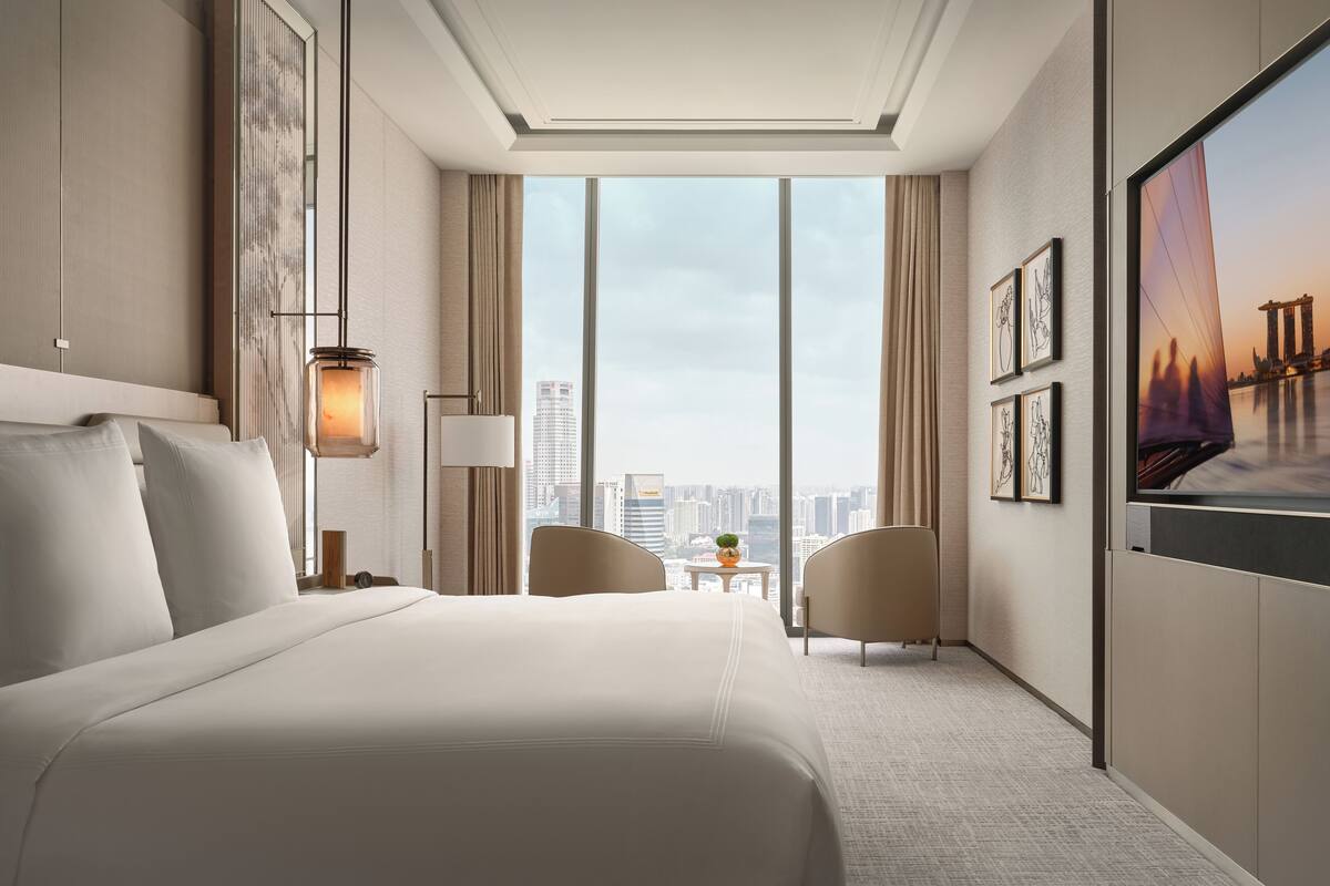 A modern hotel room with a large bed, a desk, a chair, and a city view.