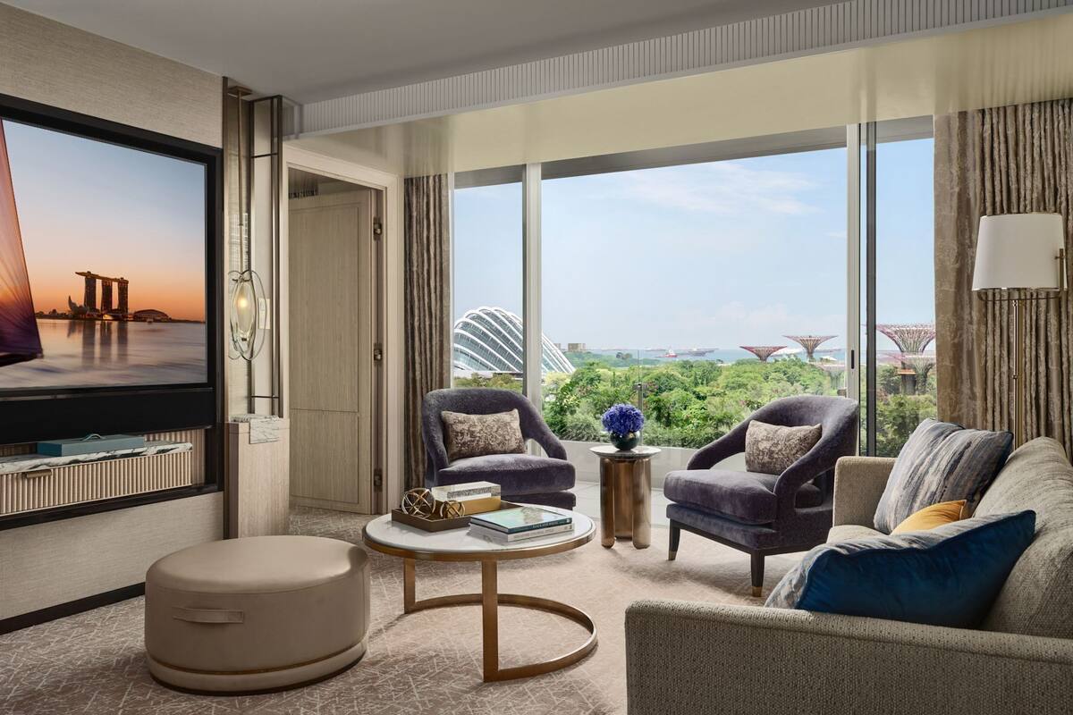 A modern hotel room with a large TV, comfortable seating, a coffee table, and a view of a cityscape.