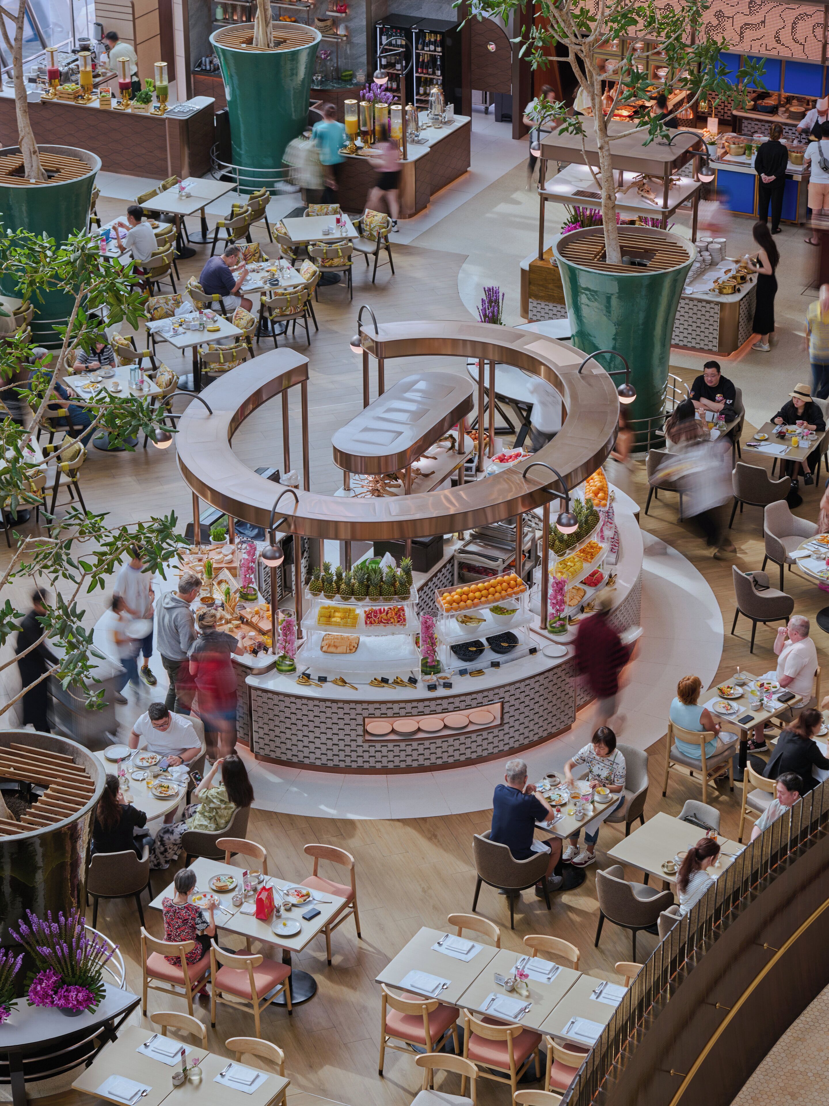 A spacious indoor dining area with multiple seating arrangements, a central buffet, and a variety of plants and decorative elements.