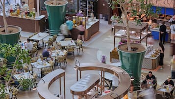 A spacious indoor dining area with multiple seating arrangements, a central buffet, and a variety of plants and decorative elements.
