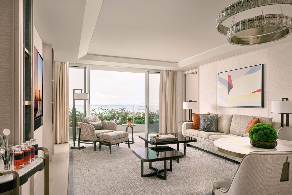 A modern hotel room with a large balcony, a sofa, a coffee table, and a chandelier.