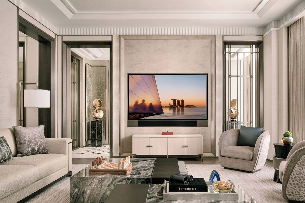 A modern living room with a large flat-screen TV, a sofa, a coffee table, and a bookshelf.