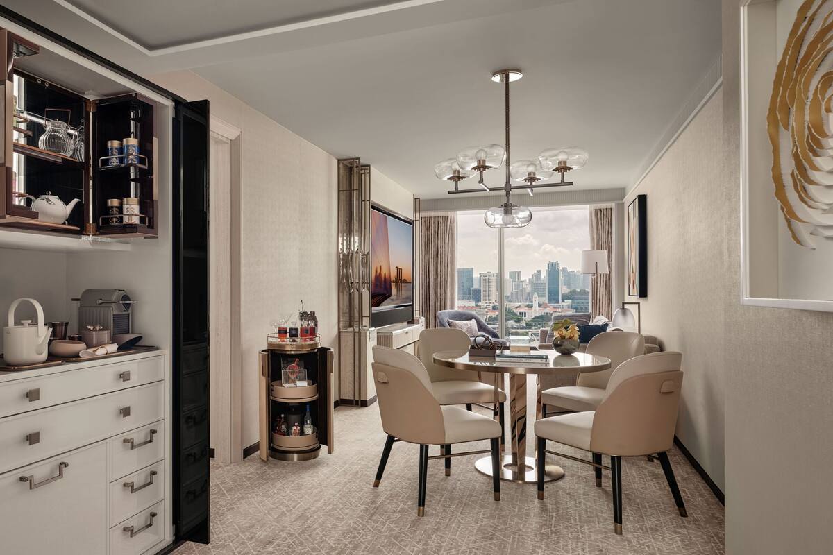 A modern dining area with a round table, beige chairs, and a city view through large windows.