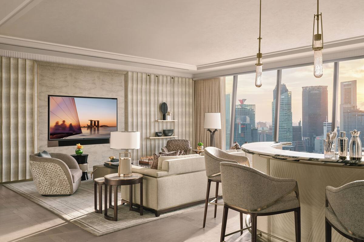 A modern hotel room with a city view, a large flat-screen TV, a bar area, and a seating arrangement.