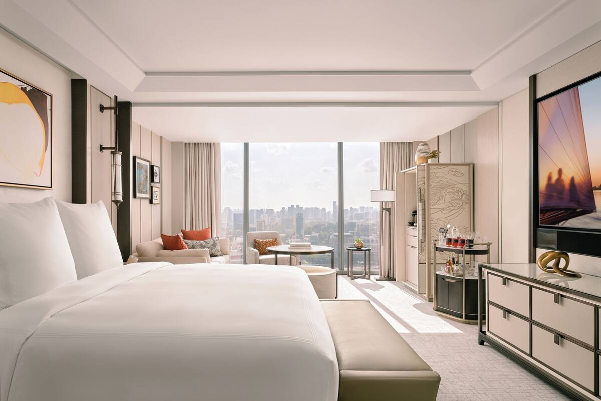 A modern hotel room with a large bed, a seating area with a sofa and armchairs, a small table, and a TV.