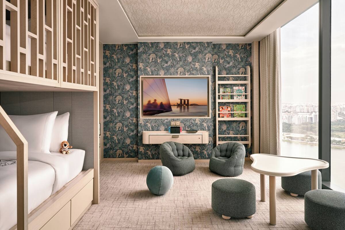 A modern bedroom with a bunk bed, a desk, bean bags, and a view of the city.