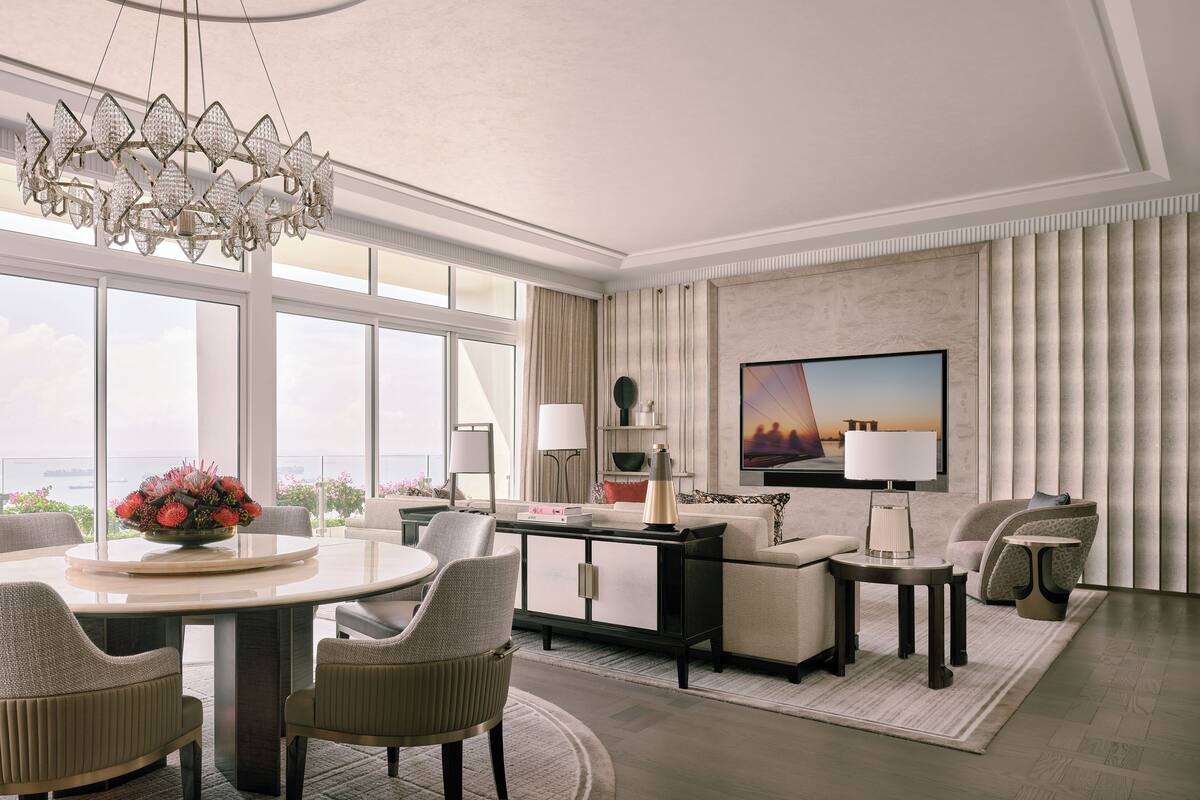 A modern living room with a large window, a chandelier, a flat-screen TV, and a dining area.