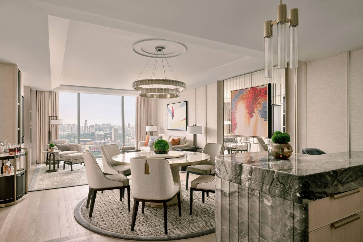 A modern hotel room with a marble dining table, comfortable seating, a city view, and a large abstract painting.