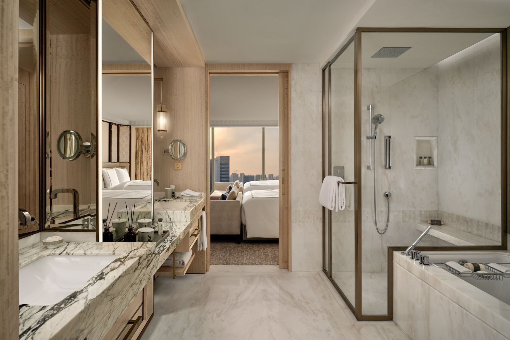 A modern hotel bathroom with a marble vanity, a separate shower area, and a view of the cityscape through an open door.
