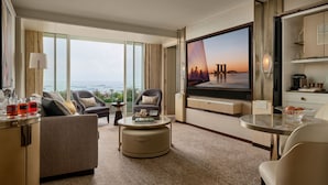 Amplia habitación de hotel con televisor grande, asientos cómodos, zona de comedor y vistas a la ciudad.