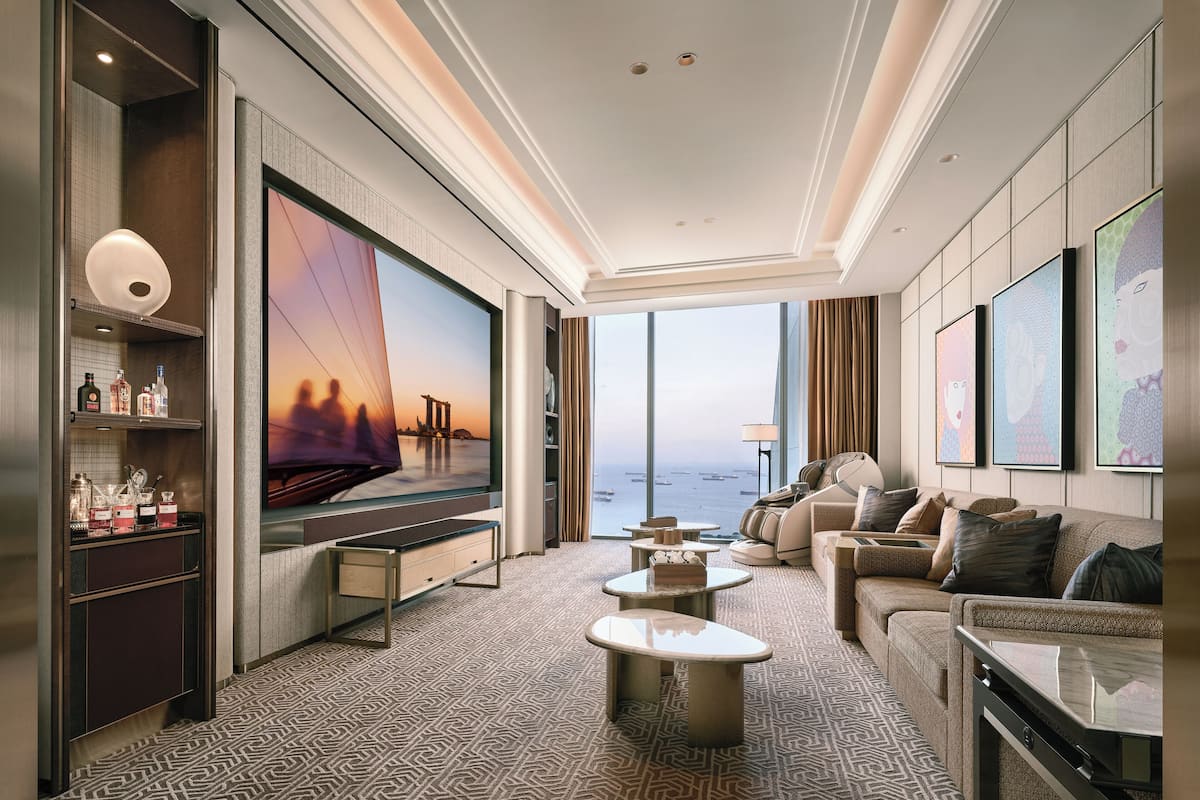 A modern hotel room with a large TV, comfortable seating, a minibar, and a view of the sea.
