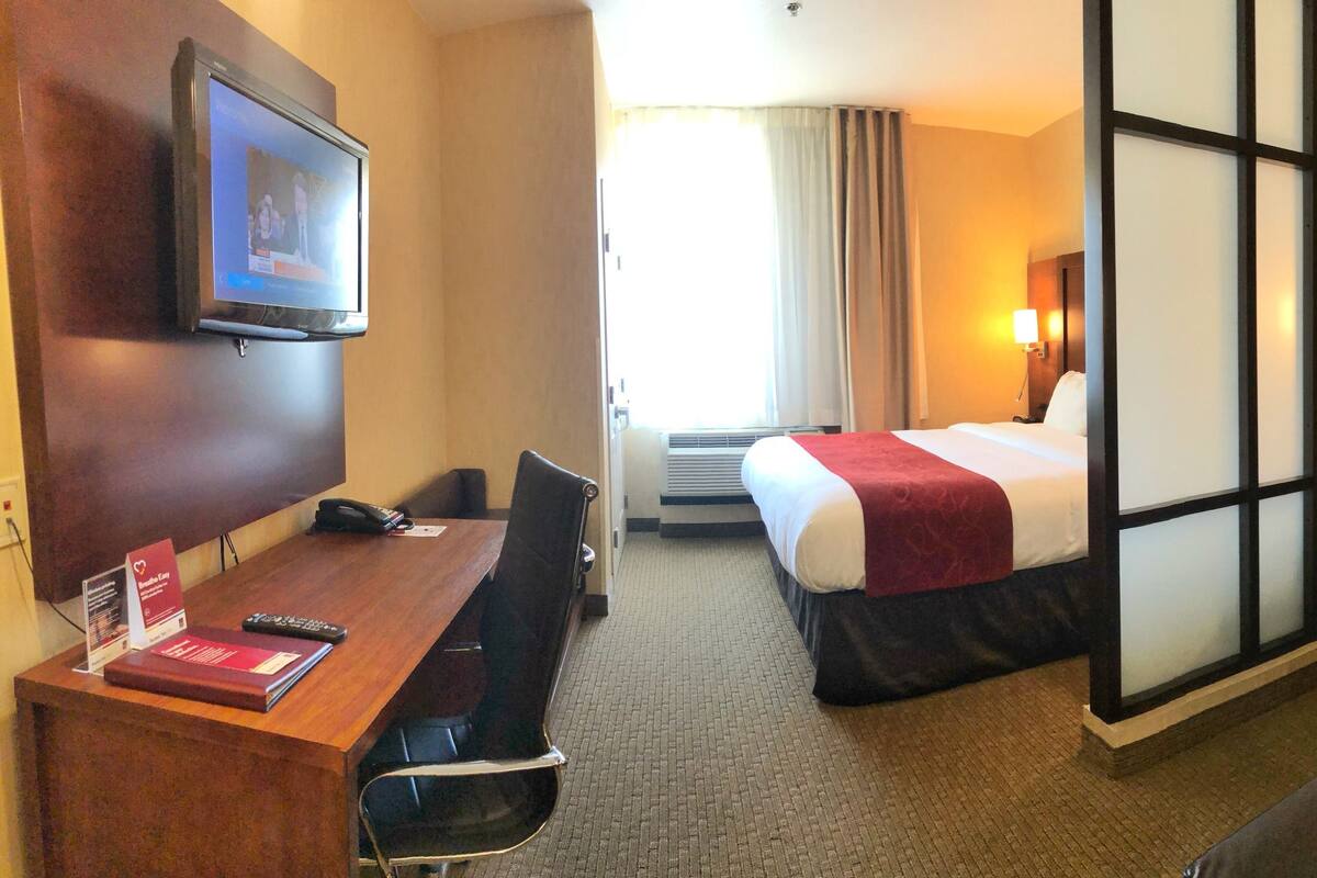 A hotel room with a desk, a bed, a sofa, a TV, and framed pictures on the wall.