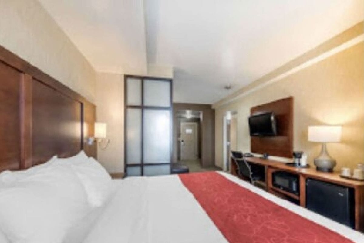 Ein Hotelzimmer mit einem Bett, einem Schreibtisch, einem Fernseher und einer Tür zu einem anderen Raum.