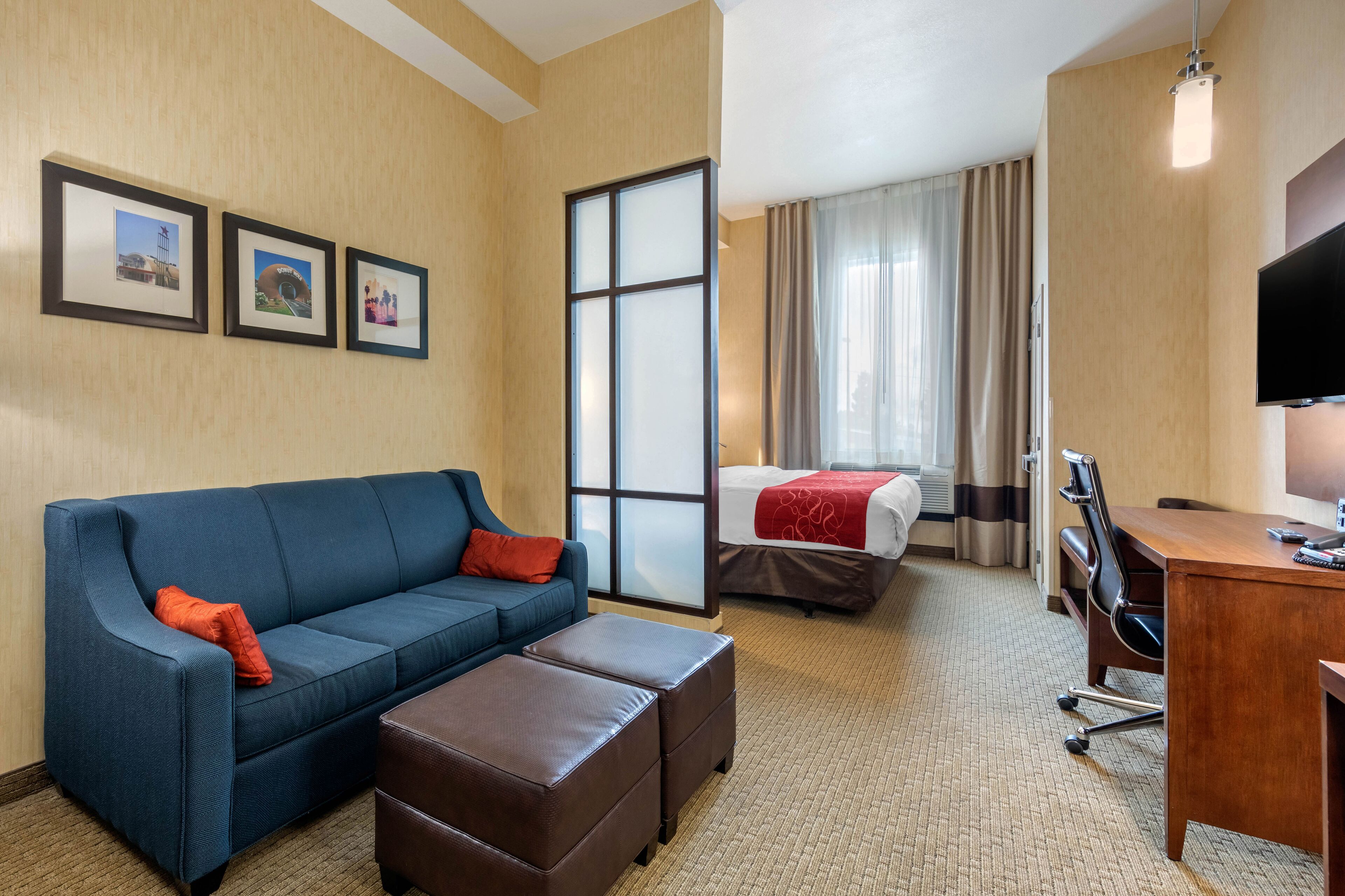 A hotel room with a blue sofa, a wooden desk, a bed with a red blanket, and a TV.
