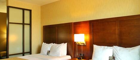 A hotel room with two beds, a nightstand, a lamp, and a mirror.