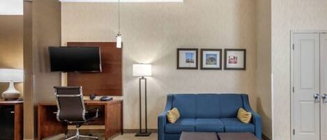 Habitación de hotel con escritorio, silla, televisión, sofá azul y una puerta.