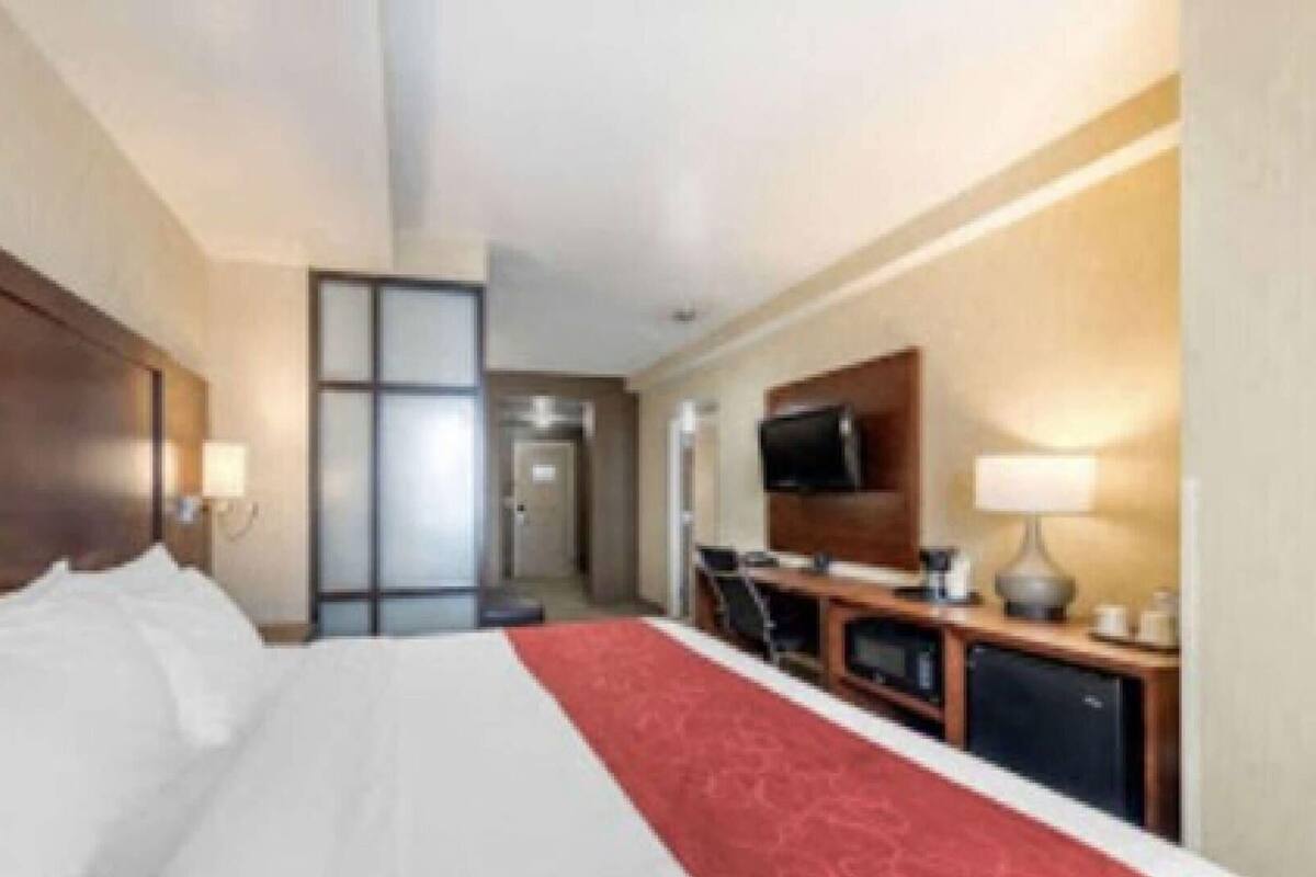 A hotel room with a bed, a desk, a television, and a door leading to another room.