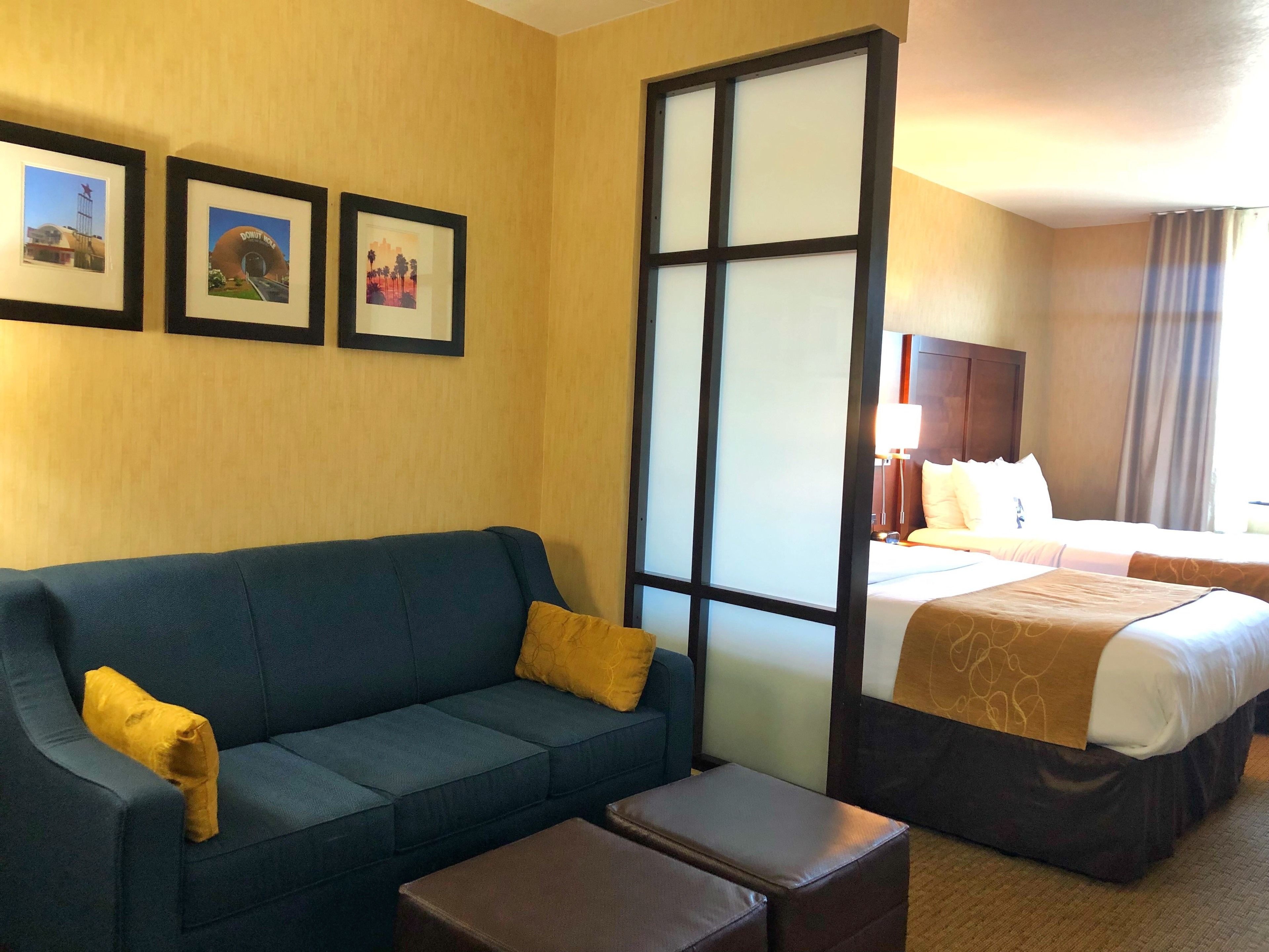 Une chambre d’hôtel avec un canapé bleu, une petite table, un lit recouvert d’une courtepointe marron et trois tableaux encadrés accrochés au mur.