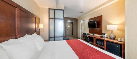 A hotel room with a large bed, a desk with a computer, a microwave, and a television.