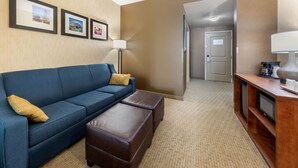 A hotel room with a blue sofa, a wooden coffee table, a lamp, and framed pictures on the wall. - Comfort Suites Near City of Industry - Los Angeles (La Puente)